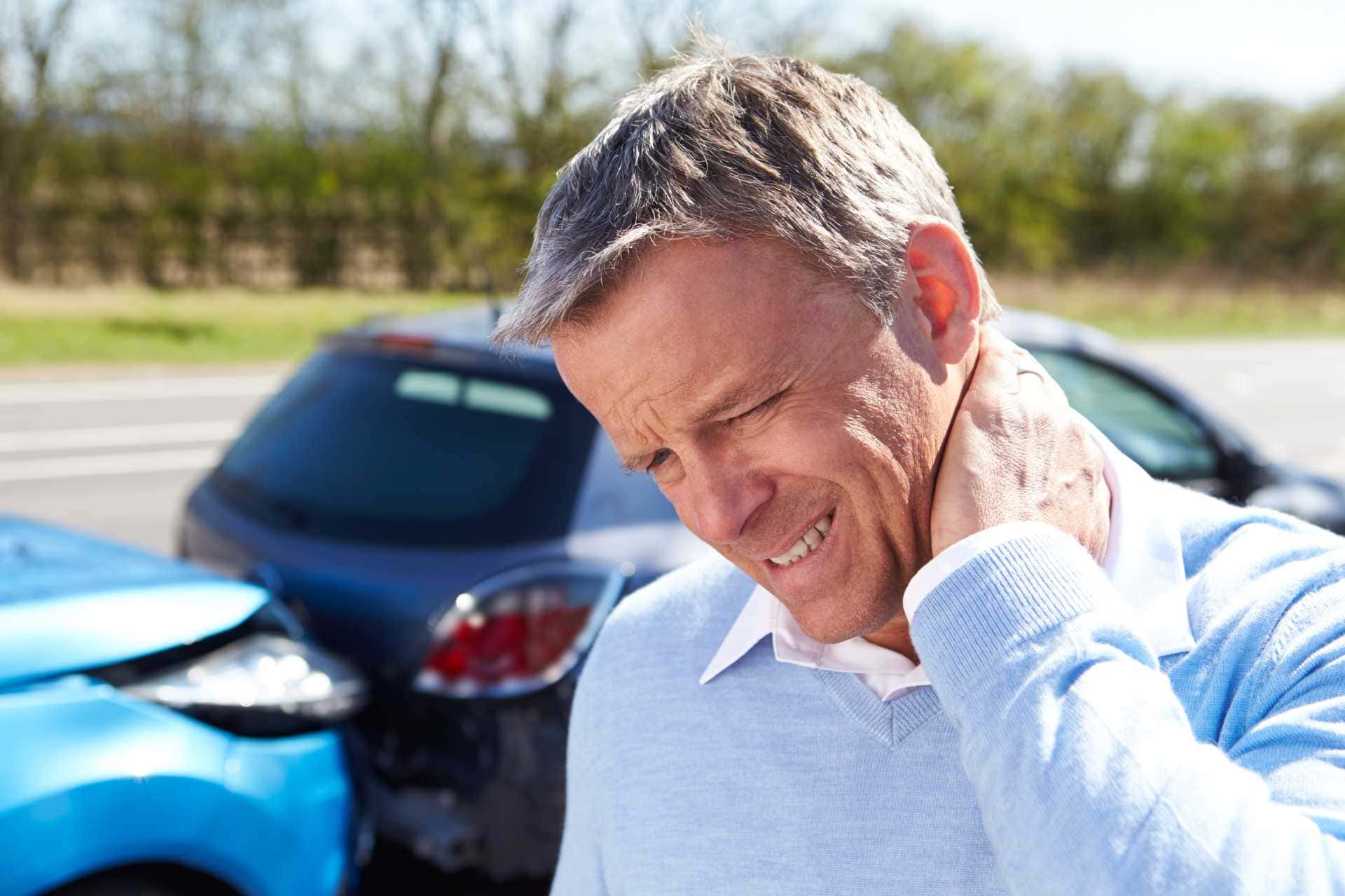 Man holding neck next to car accident