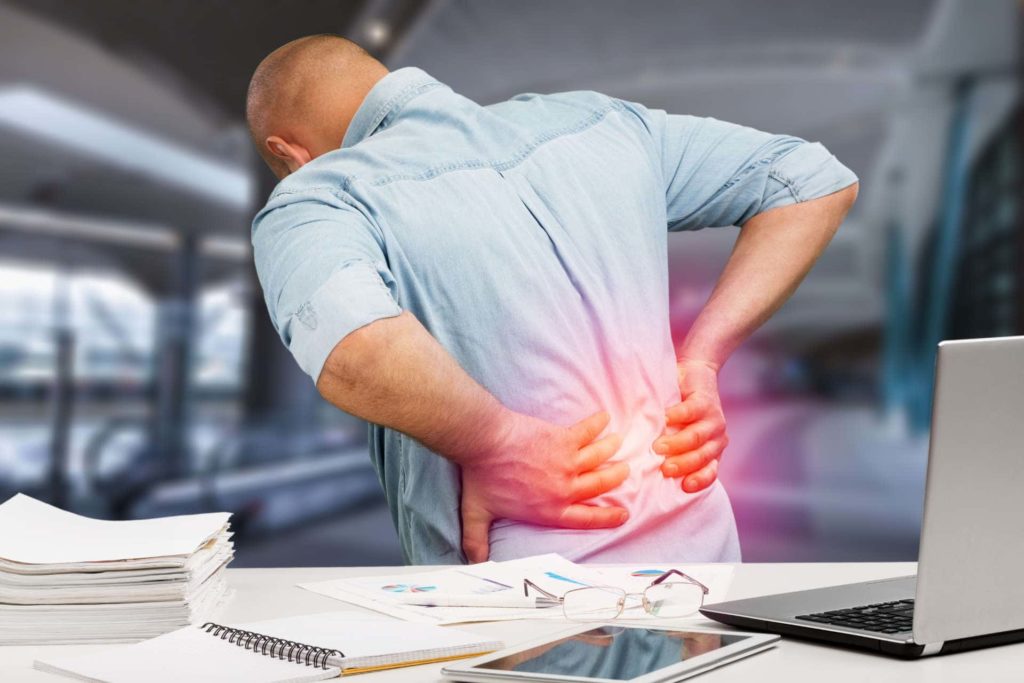 office worker at desk holding lower back in pain